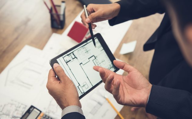 Real estate agent with client or architect team discussing a housing model and its blueprints digitally using a tablet computer
